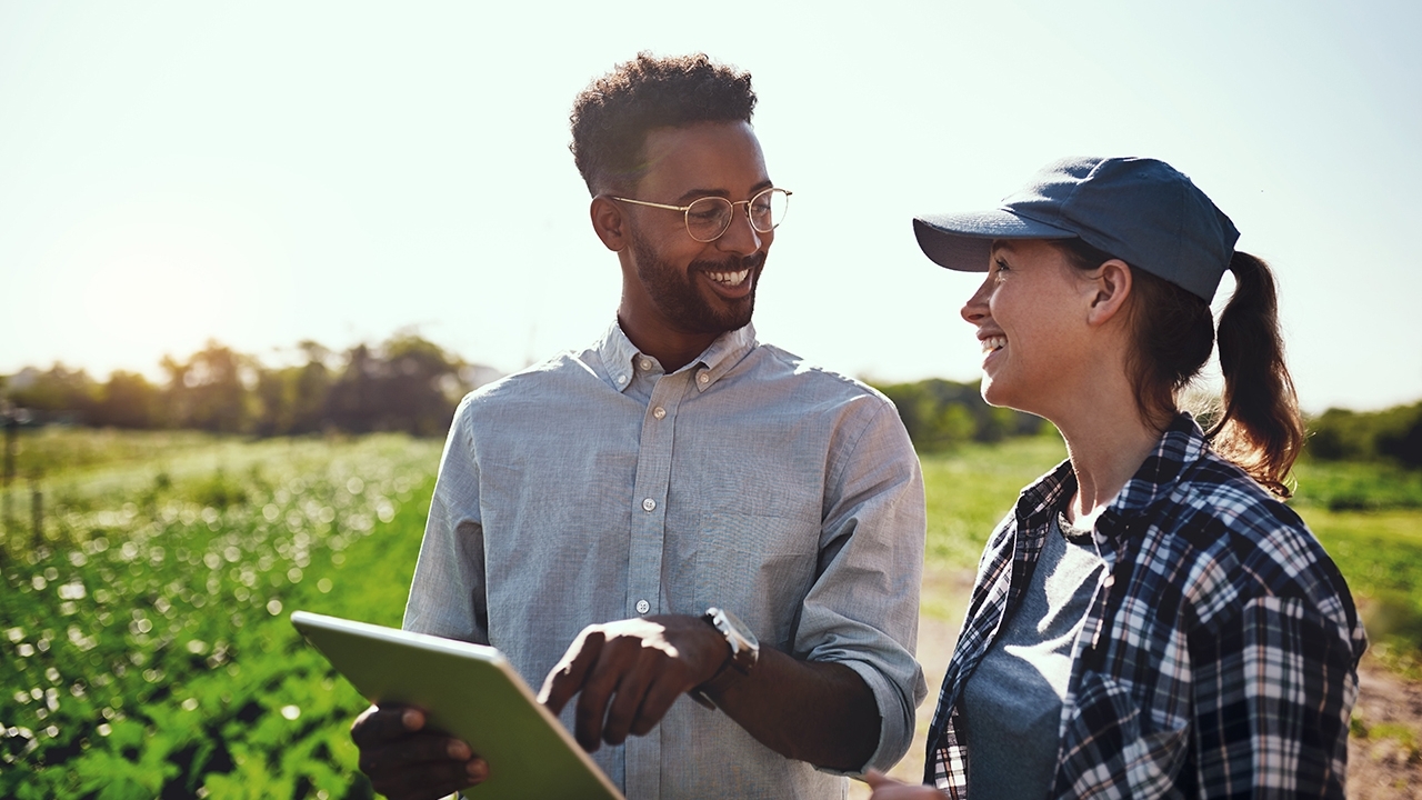 Two people in field.  Man holding a clip board.