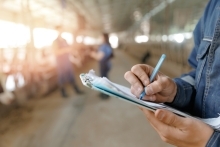 close up image of person holding a clipboard with works inside of barn in background